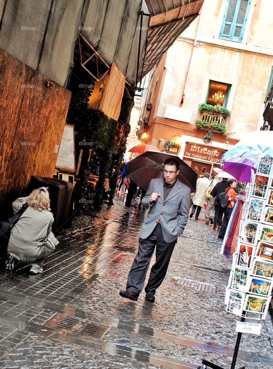 Thinkin in the rain. A man looks lost in thought as he strolls the rain slicked cobblestone street under his umbrella in Rome
