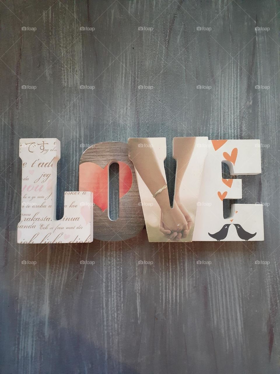 The word Love in wooden lettering on a wooden table. There are pictures in each letter that represents love.