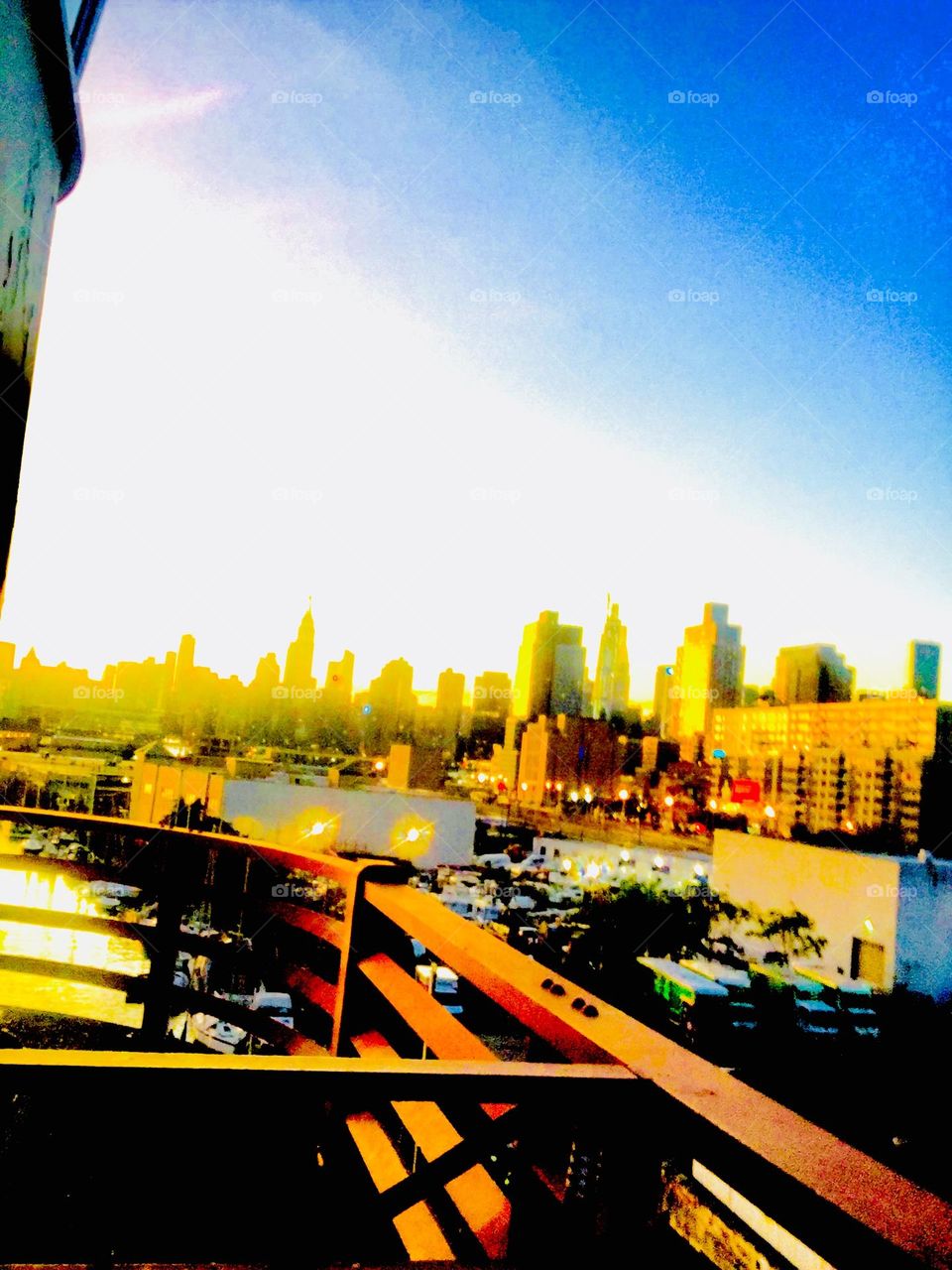 The Manhattan skyline seen far in the distance during the „golden hour“ of sunset on a clear summer evening. This photo was taken from the top of the Pulaski Bridge in LIC, Queens, NY. Hypnotic Productions
