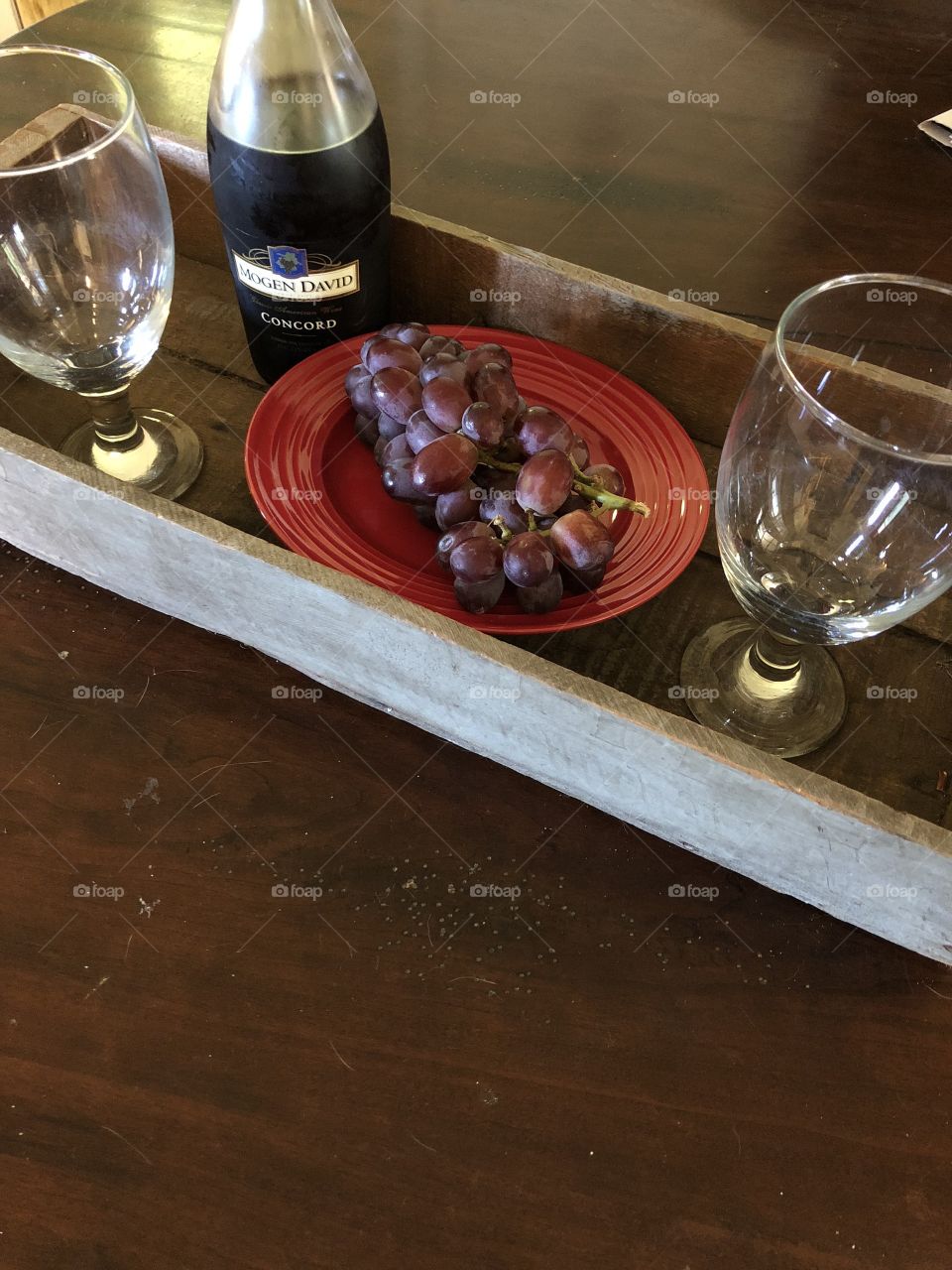 Old vintage tray displaying bottle of wine. Two empty glasses and purple red grapes. 