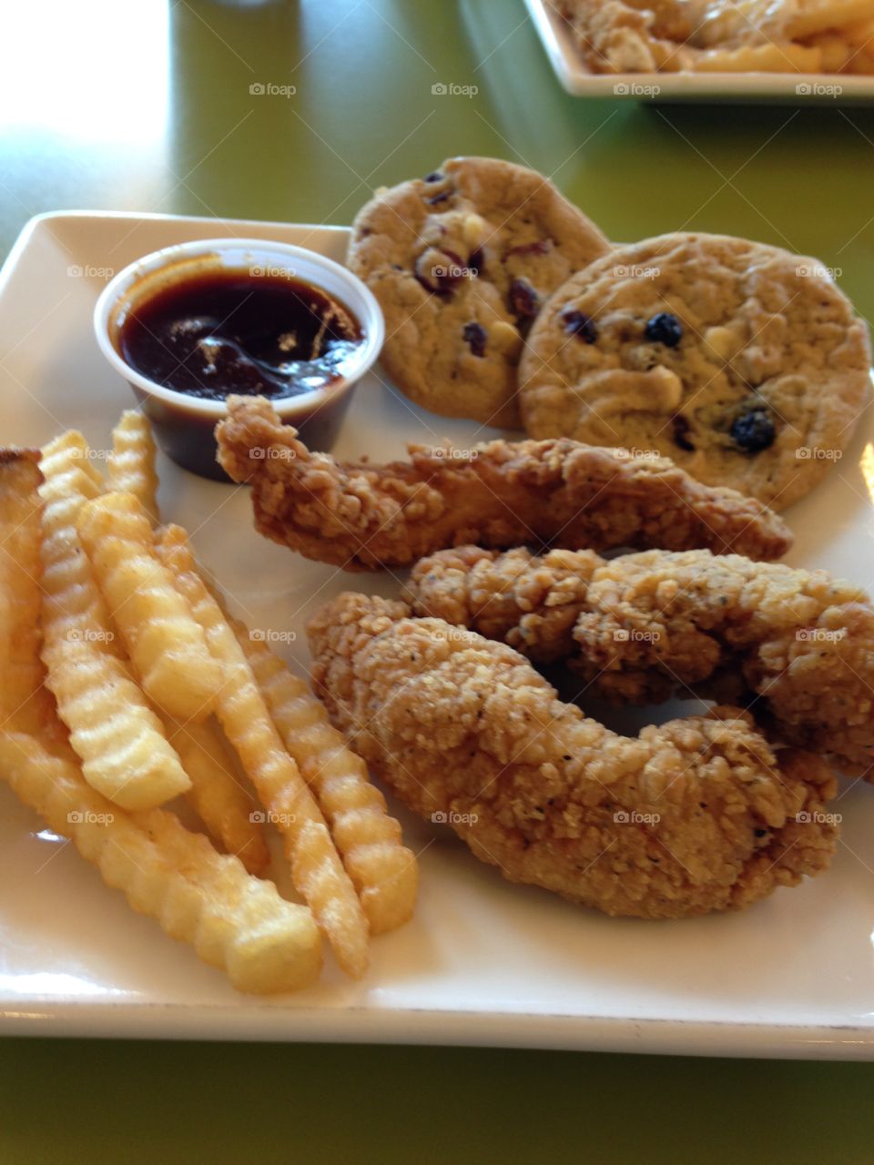 Plate of fried foods including breaded chicken tenders, crinkle cut French fries, and chocolate chip cookies 