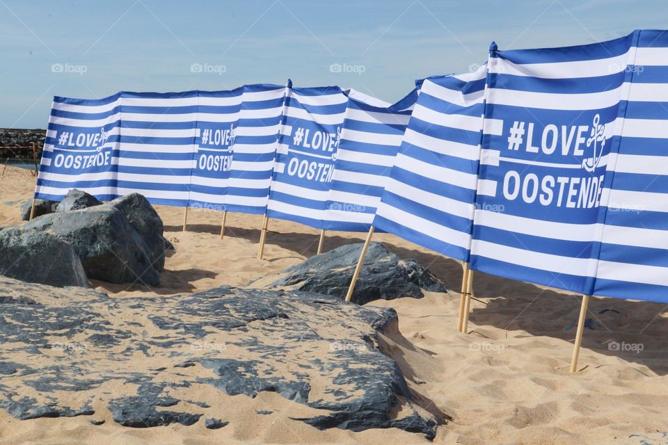 Beautiful side view of a long textile banner in blue and white stripes with the hashtag love oostend on the sandy rocky shore of the north sea in belgium, close-up side view. The concept of beautiful nautical backgrounds and wallpapers.