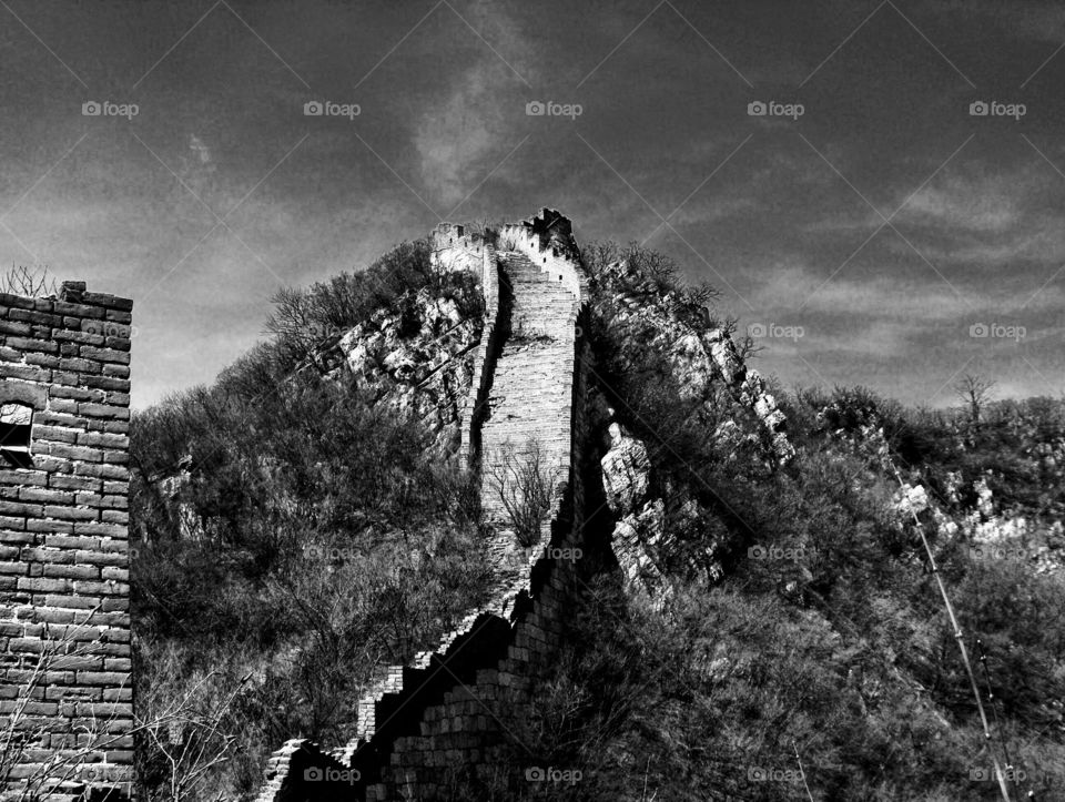 Black and white image of the ruins of the Great Wall of China rising up to a peak 