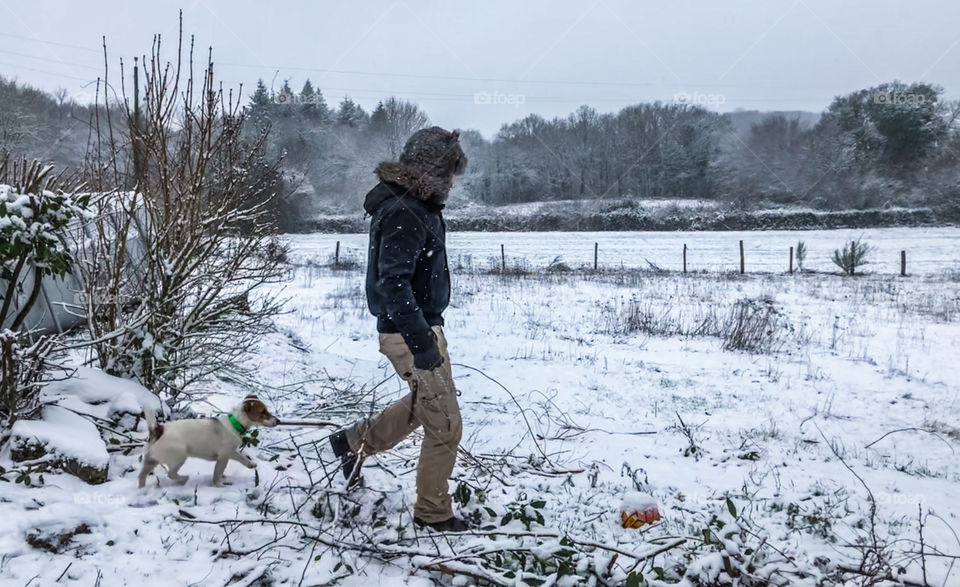 A man, wrapped up warm, walks his dog in the winter snowy landscape 