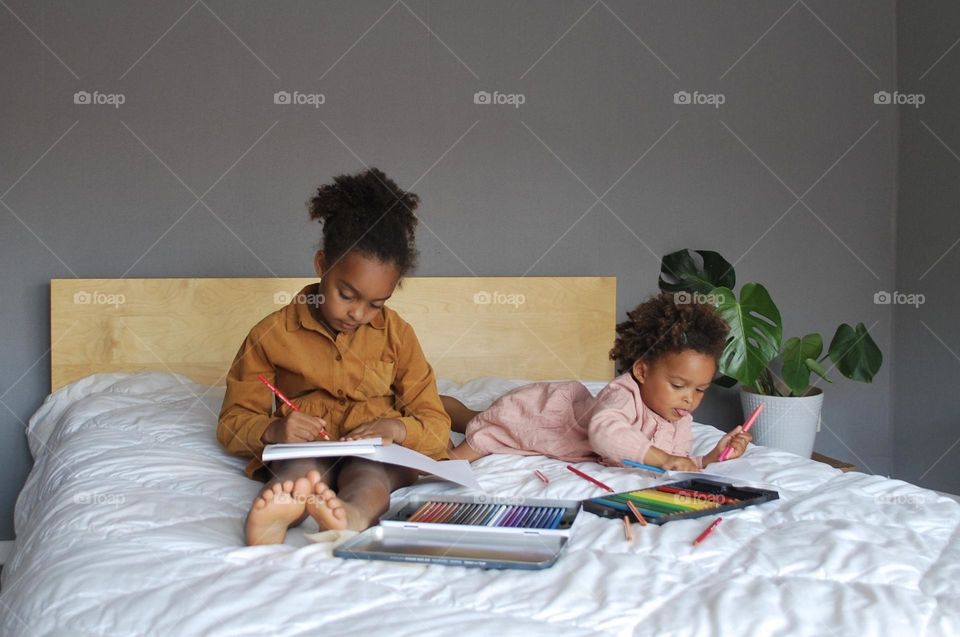 Two little girls of mixed race coloring in bed