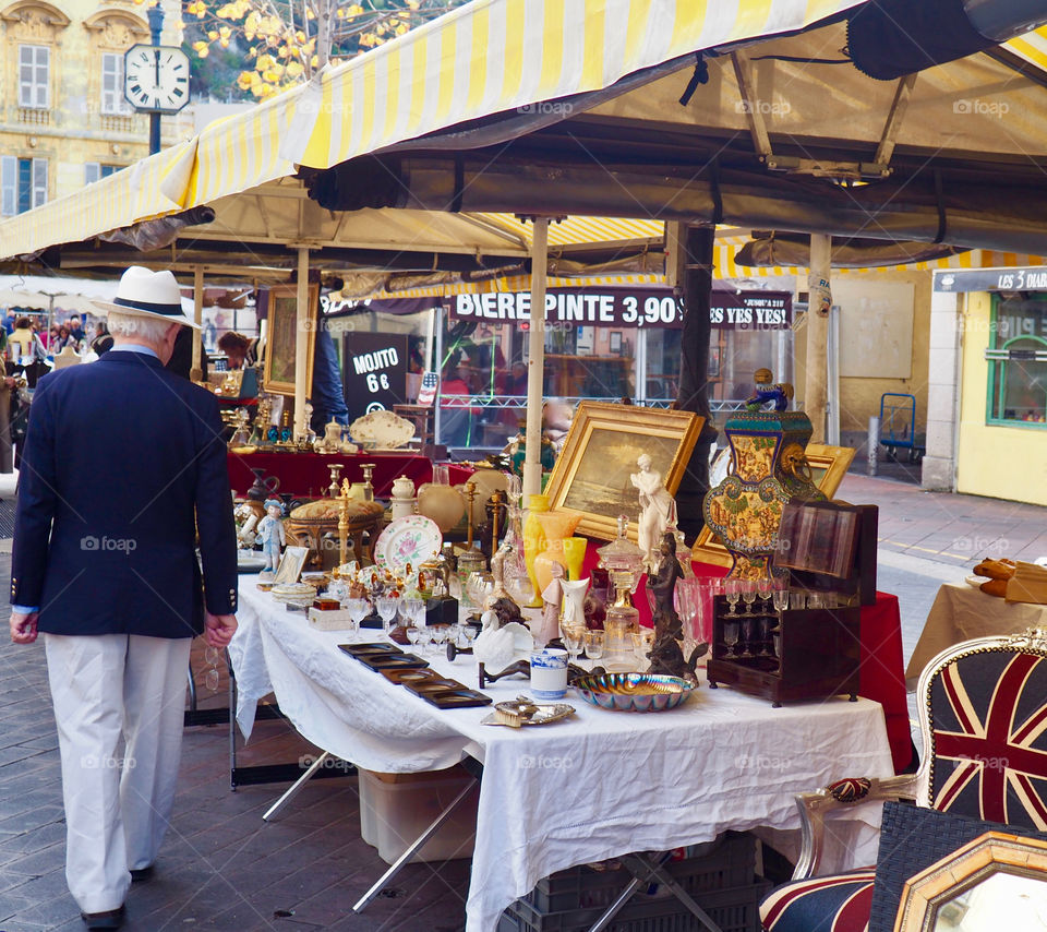 Elegant elderly man in hat with back turned looking at the antiques market on the Cours Saleya in Nice, France.