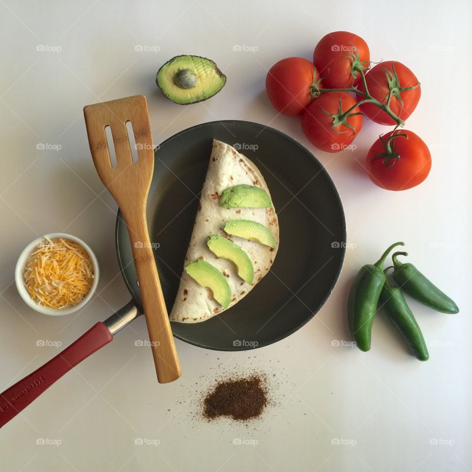 Homemade burrito in skillet with spatula and ingredients. 