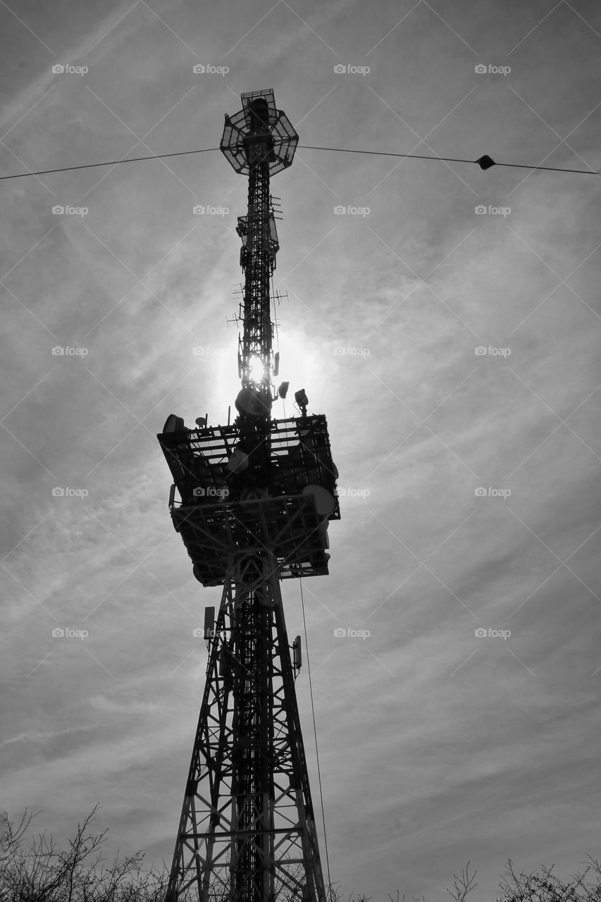 Shot from below of a large transmission tower behind which the sun is hiding