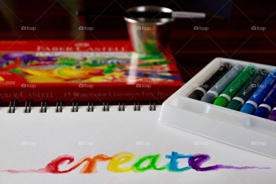 Colours of the World - watercolor crayons in white tray, brush and small stainless steel water container, product box, and the word “create” on mixed media wire-bound paper