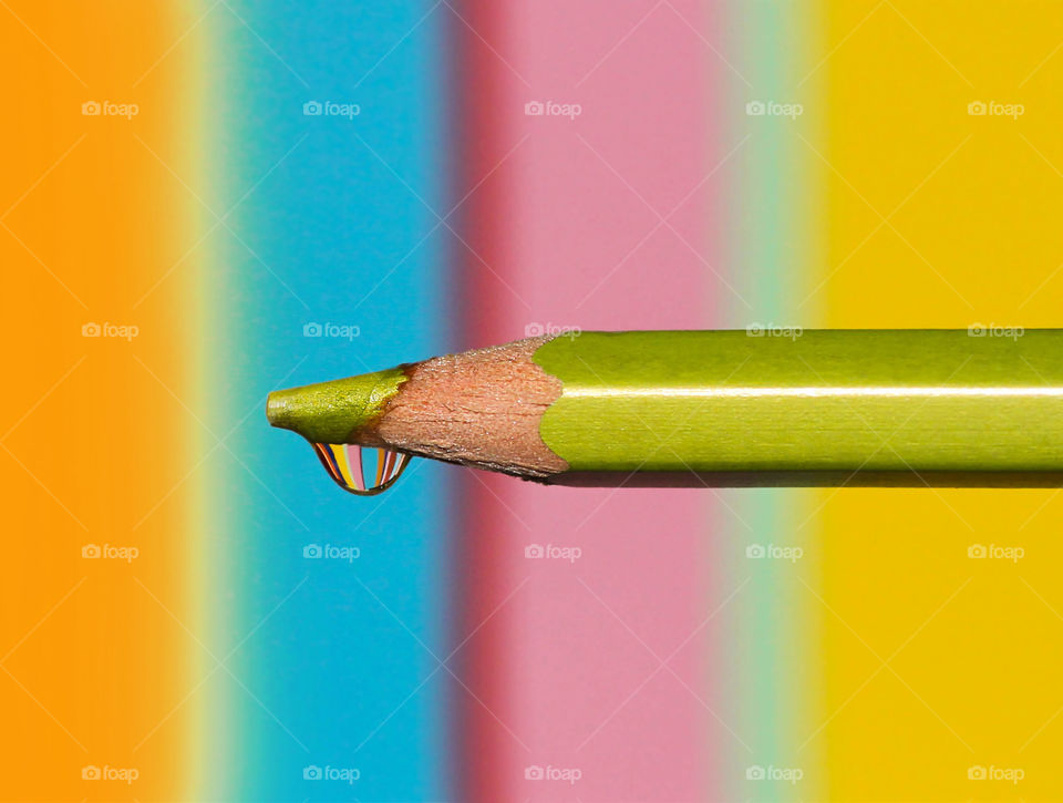 Colorful reflection in a water drop on the top of a green pencil, colorful background