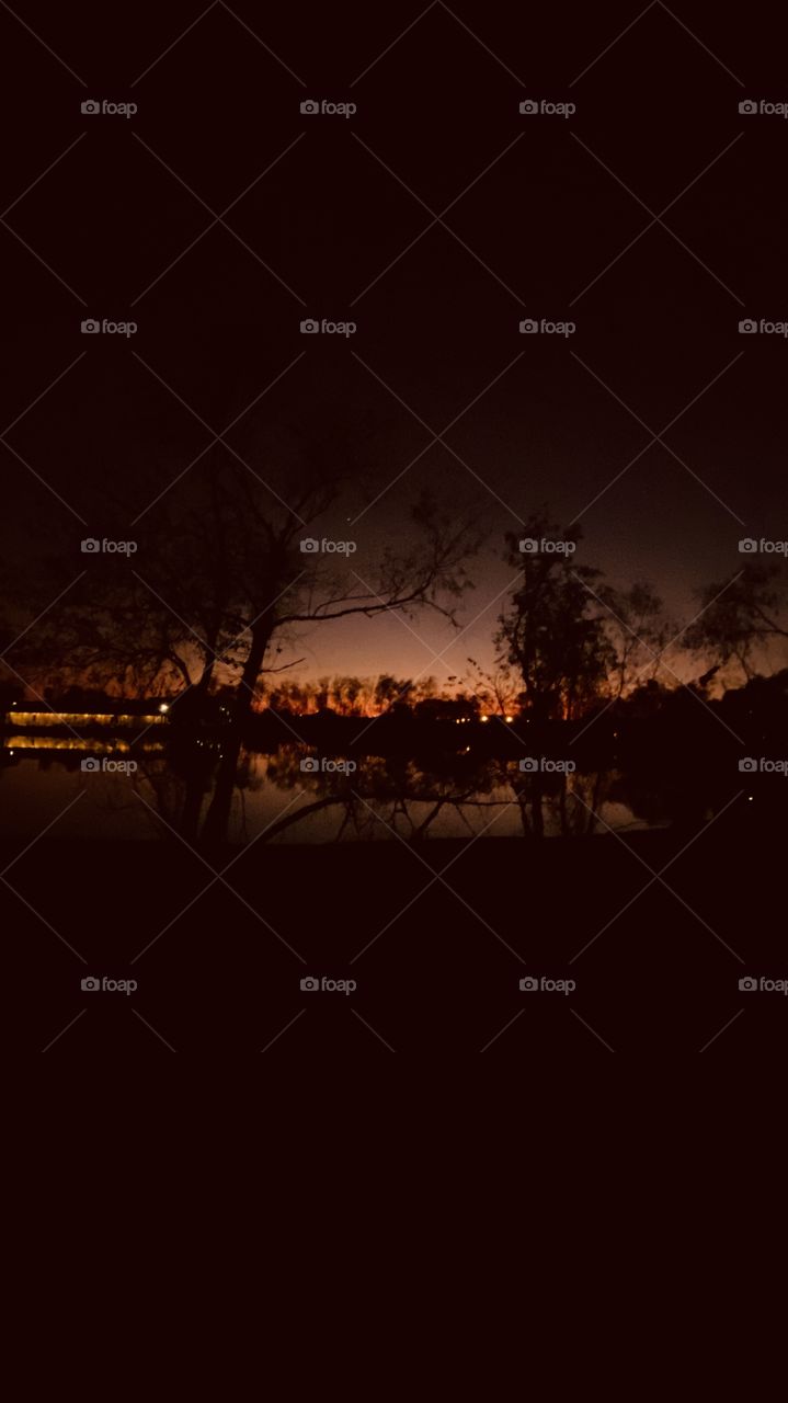 Lighthouse is gleaming that Night is near, backlit, mirrored image of lake reflections from the shore line mixed with backlit makes for a beautiful night.