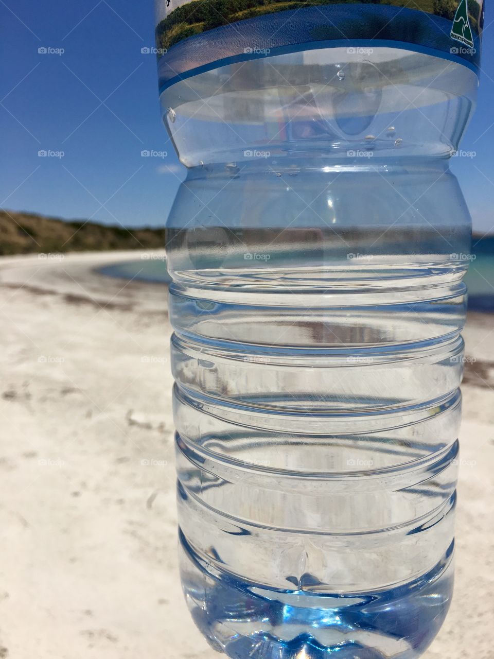 View of The ocean and shoreline through the perspective of a bottle of spring water at the beach 