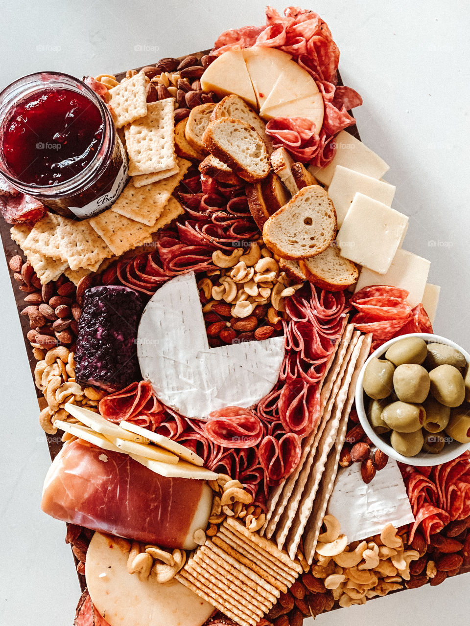 Charcuterie board filled with meats and cheeses, crackers, olives, mixed nuts (cashews, almonds) and jams.