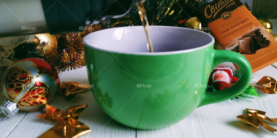 pouring tea from a thermos into a green cup on the background of a Christmas toy