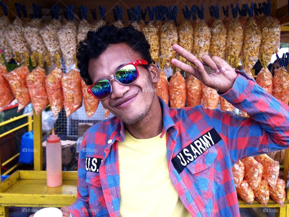 an asian man wearing sunglasses smiling and making a peace sign