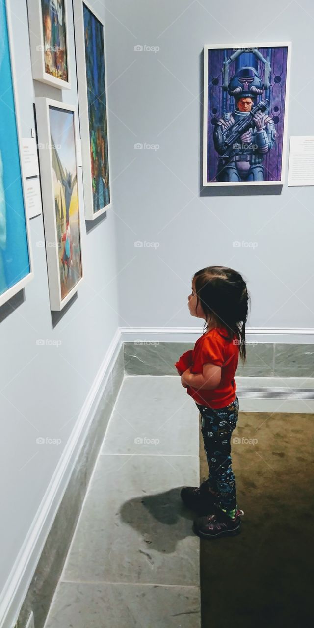 Little girl looking at picture on wall at home