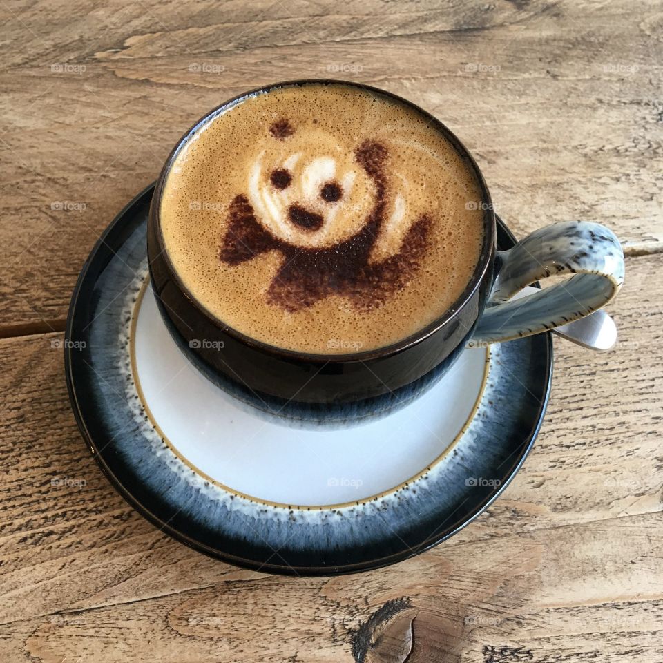 Coffee art of a panda with a rustic wooden background. 