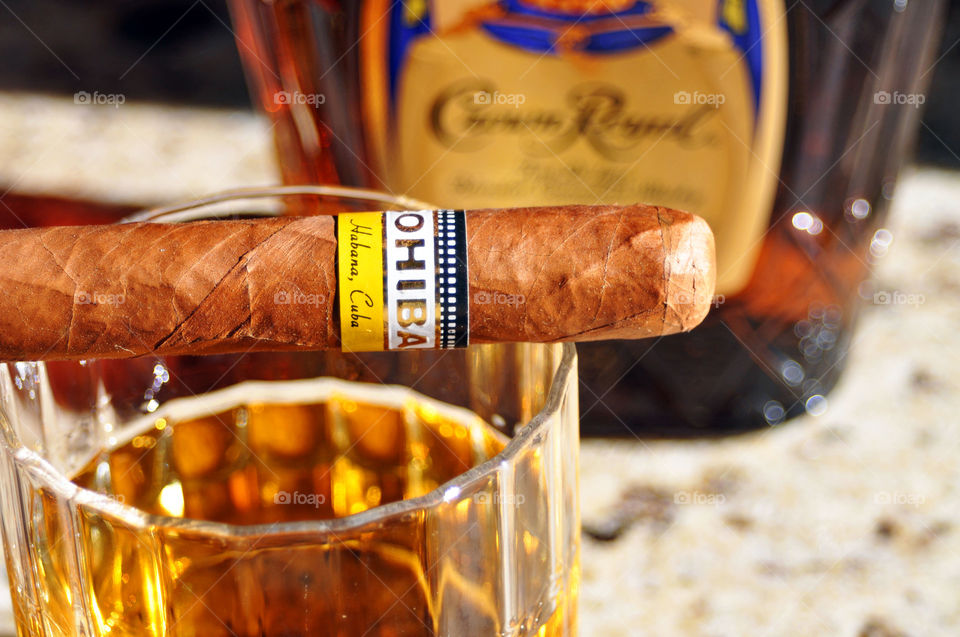 Still life. Cigar, glass of whiskey with Crown Royal bottle in the background.