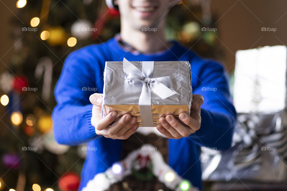 A man in a festive sweater giving a shiny gift on Christmas morning during the holiday 