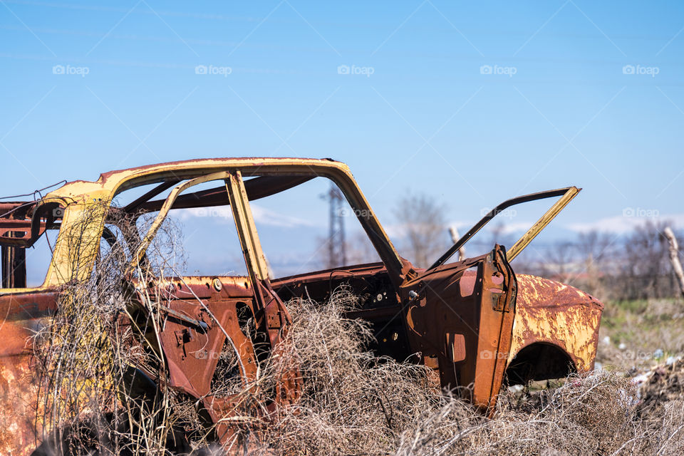 Abandoned and rusty wreckage of an yellow vintage Soviet Russian car in the middle of dry hay with scenic ice top mountains and clear blue sky on the background in rural Southern Armenia in Ararat province on 4 April 2017.