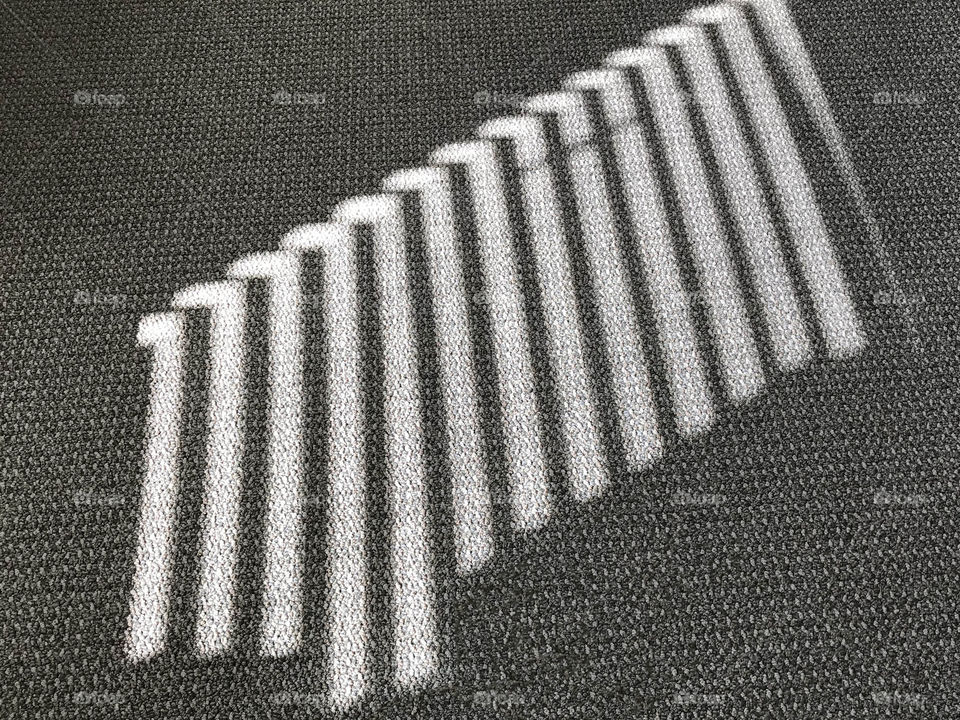 Rectangular rays of sunshine filtered through some rectangular white wooden blinds and projected onto a grey carpet!