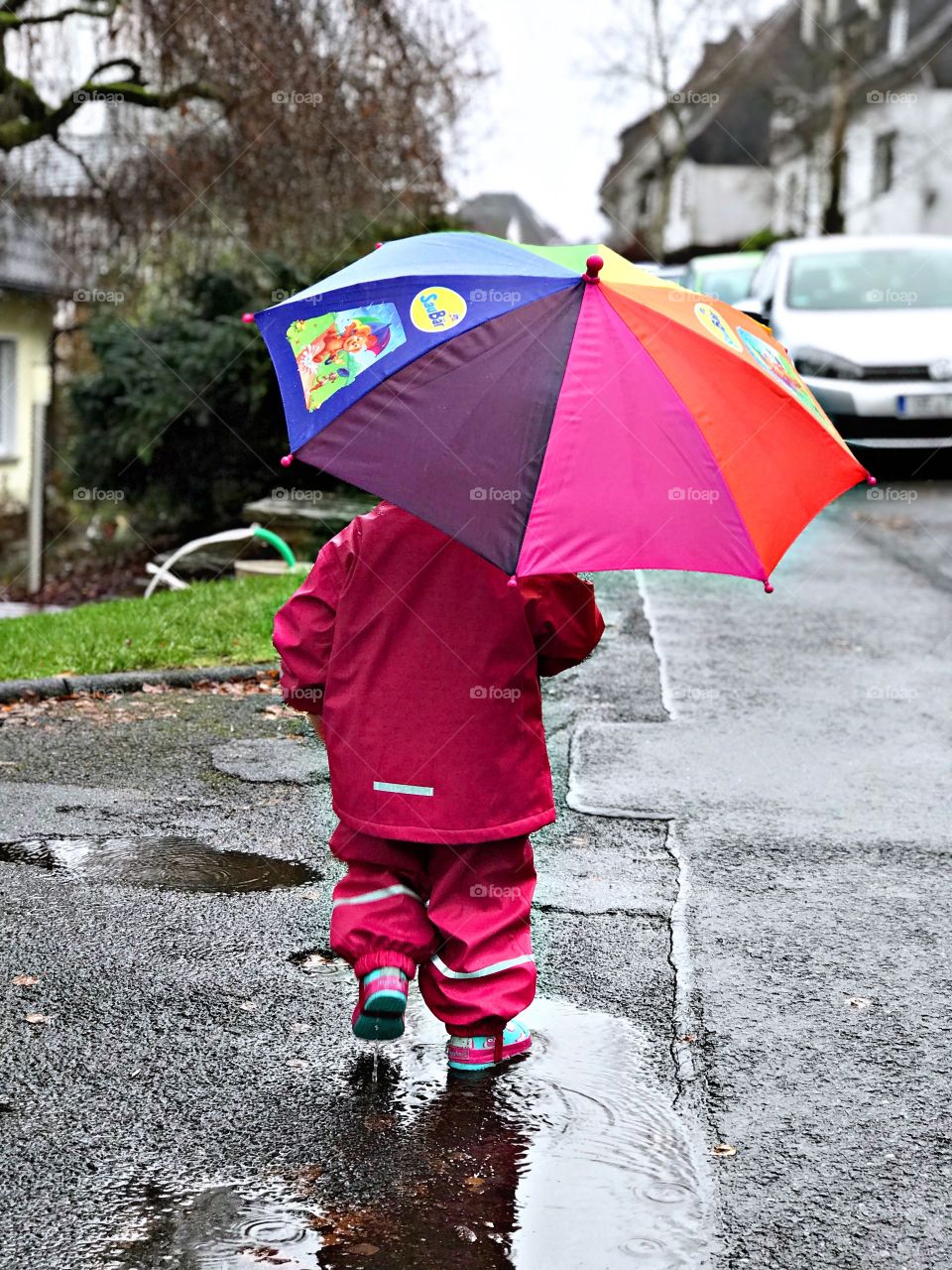 Kind läuft bei schlechtem Wetter durch Pfützen mit Regenschirm.