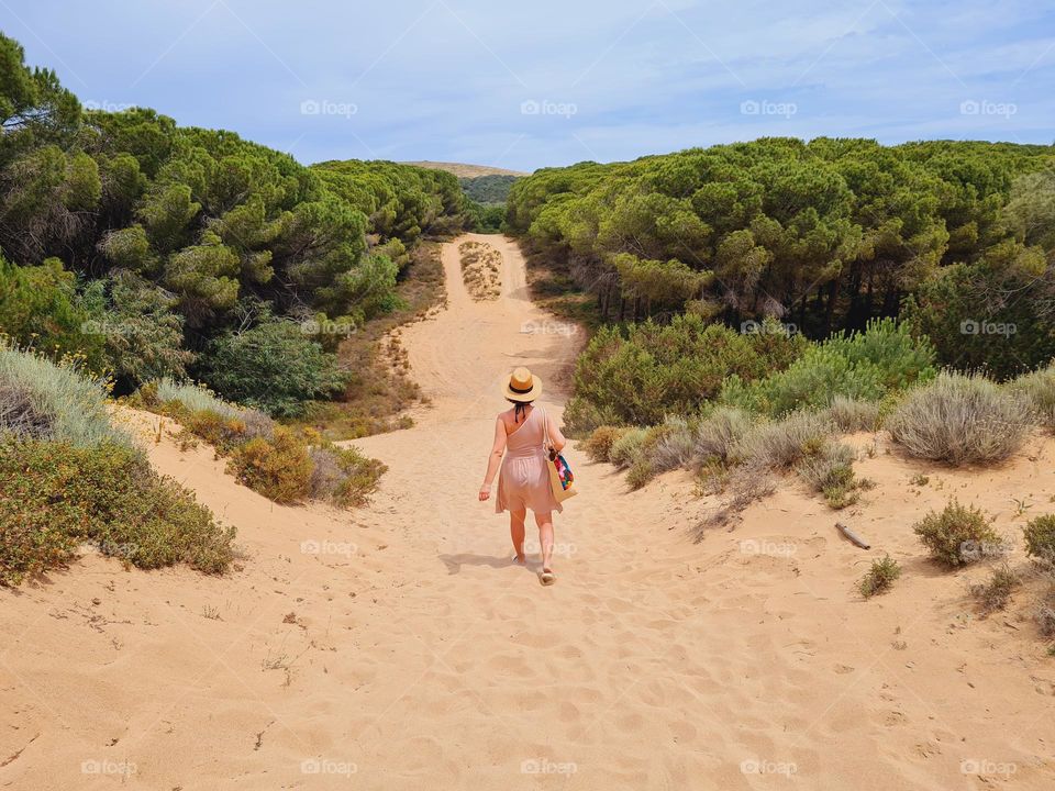 woman from behind with hat walks in the sand dunes in the wild Argentiera beach in Sardinia