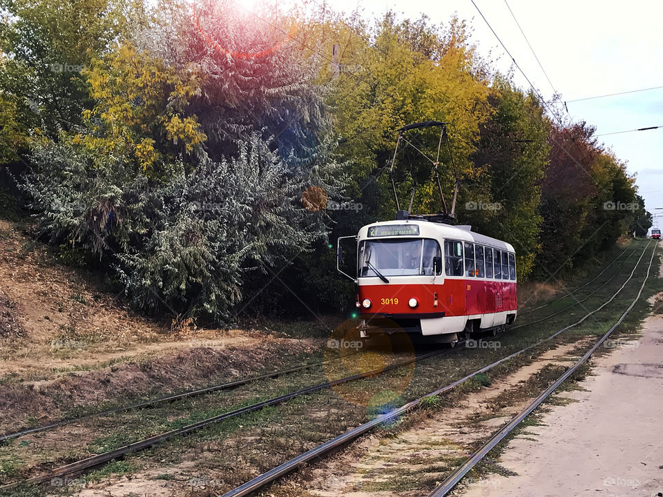 Red city tram moving in front of autumn trees by the railroad 