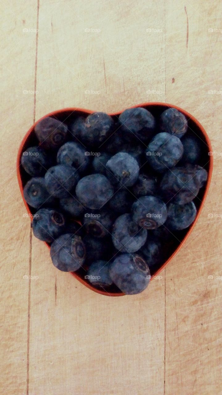 Fresh blueberries in a heart-shaped red box on wooden table