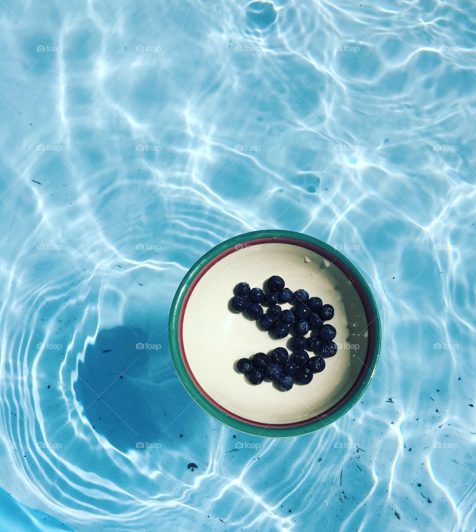 Sun reflecting off of the pool. Bowl of blueberries floating 