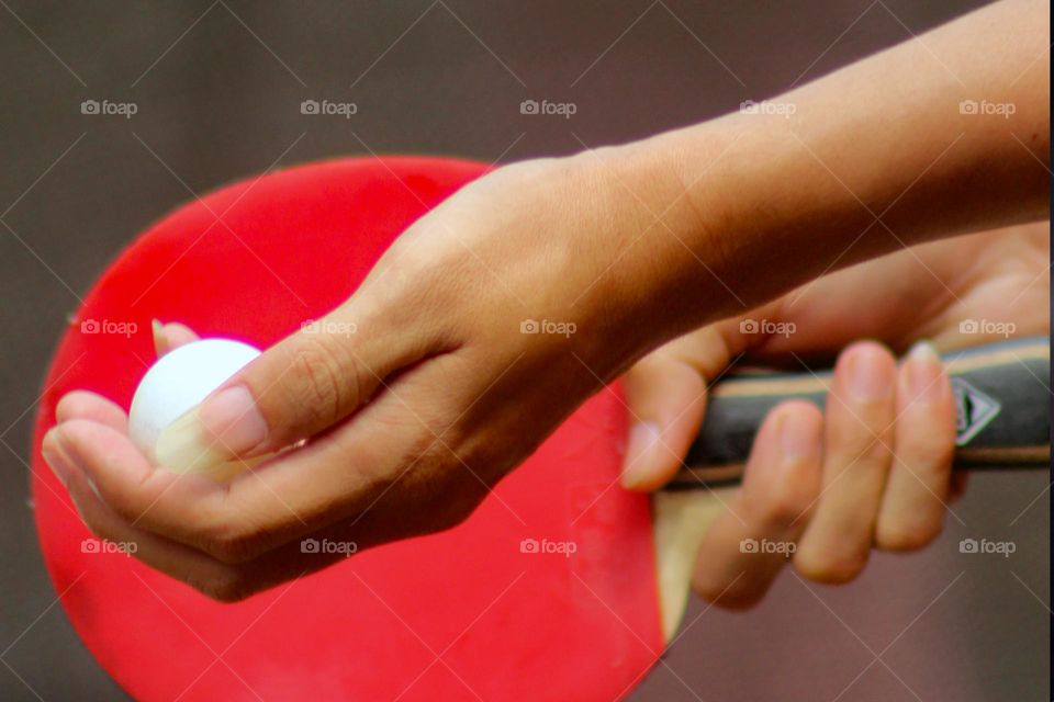 Close up of a person's hand holding a red ping-pong bet while serving in table tennis. Table tennis is one of the favorite sports in the world. Blurred Background.