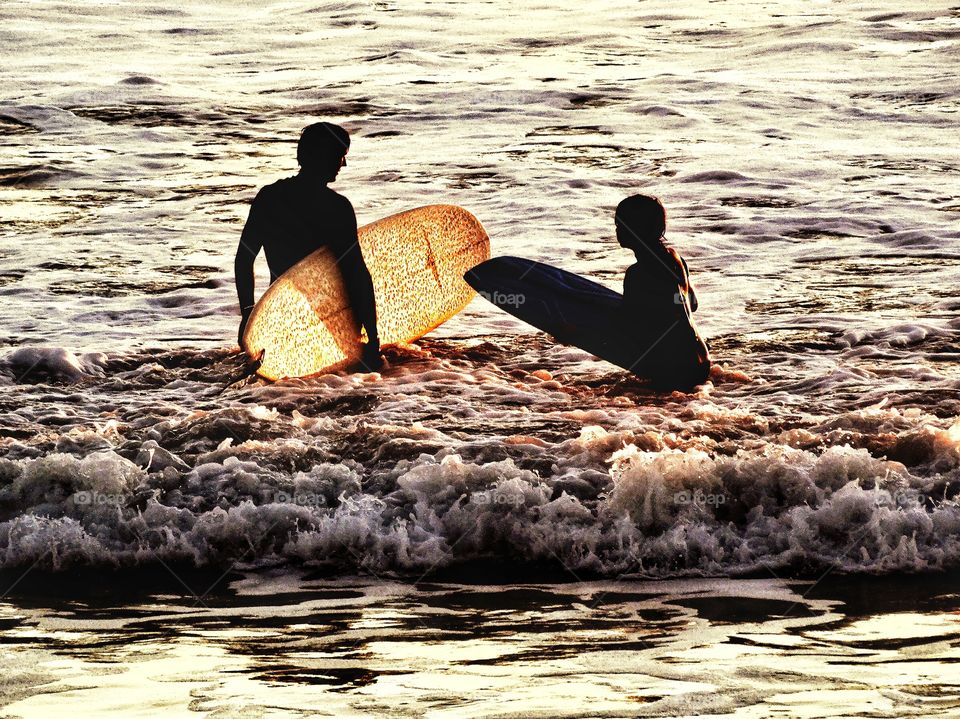 Surfing During The Golden Hour. Father And Son Surfers In The Ocean Just Before Sunset
