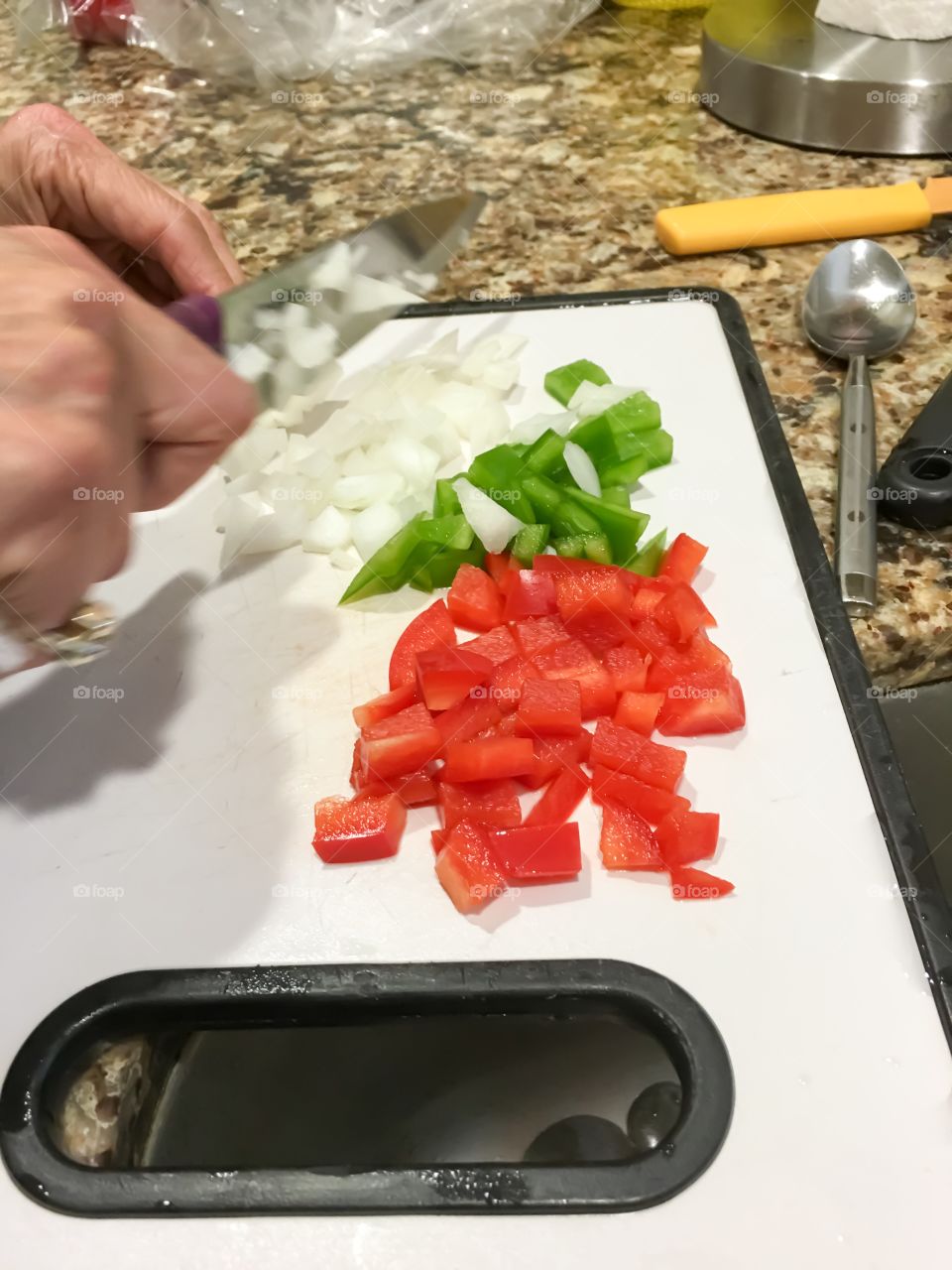 Home chef cutting capsicum sweet bell peppers and onions on cutting board hands showing