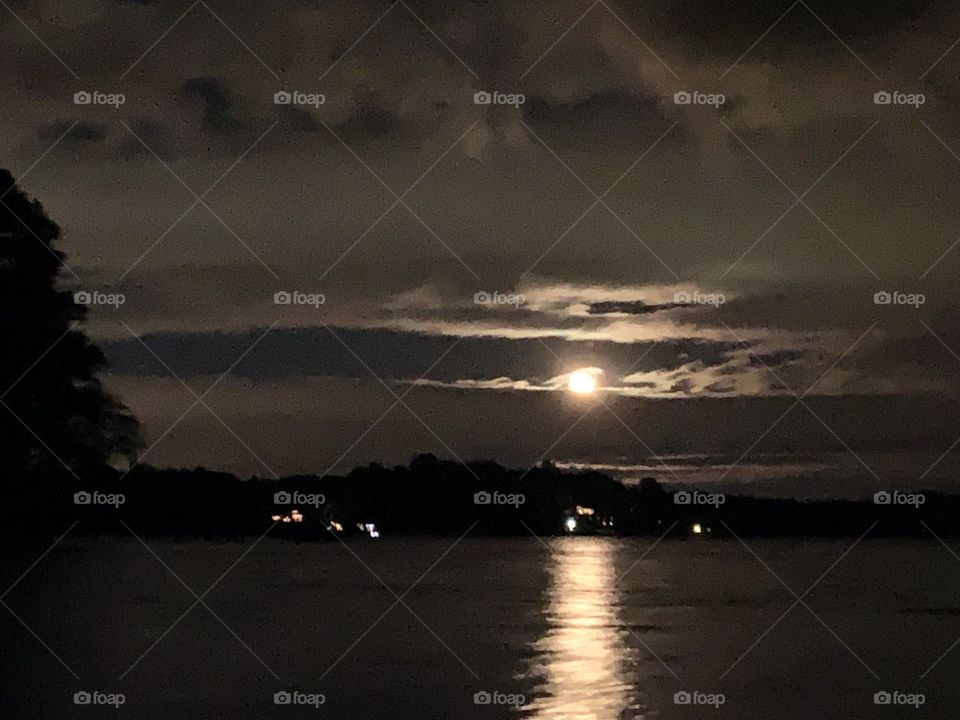 Reflection of the moon over the lake on a cloudy night with other boats