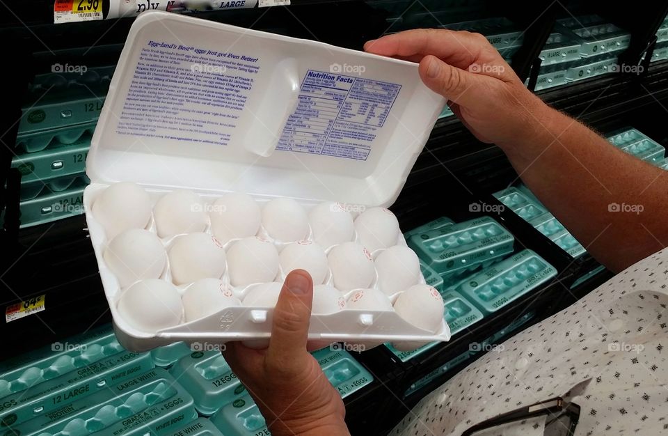 A man Shopping for eggs at the market grocery store looking at eggs in rectangular cartons