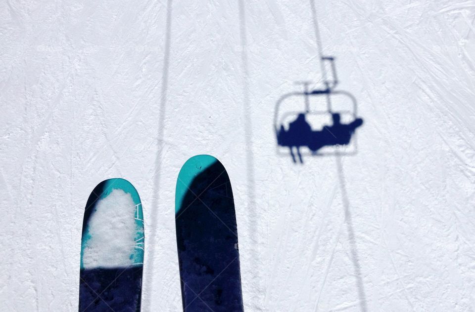 On the chairlift. Riding the chairlift on a sunny day with the shadow of the chair and skiers on the snow below.