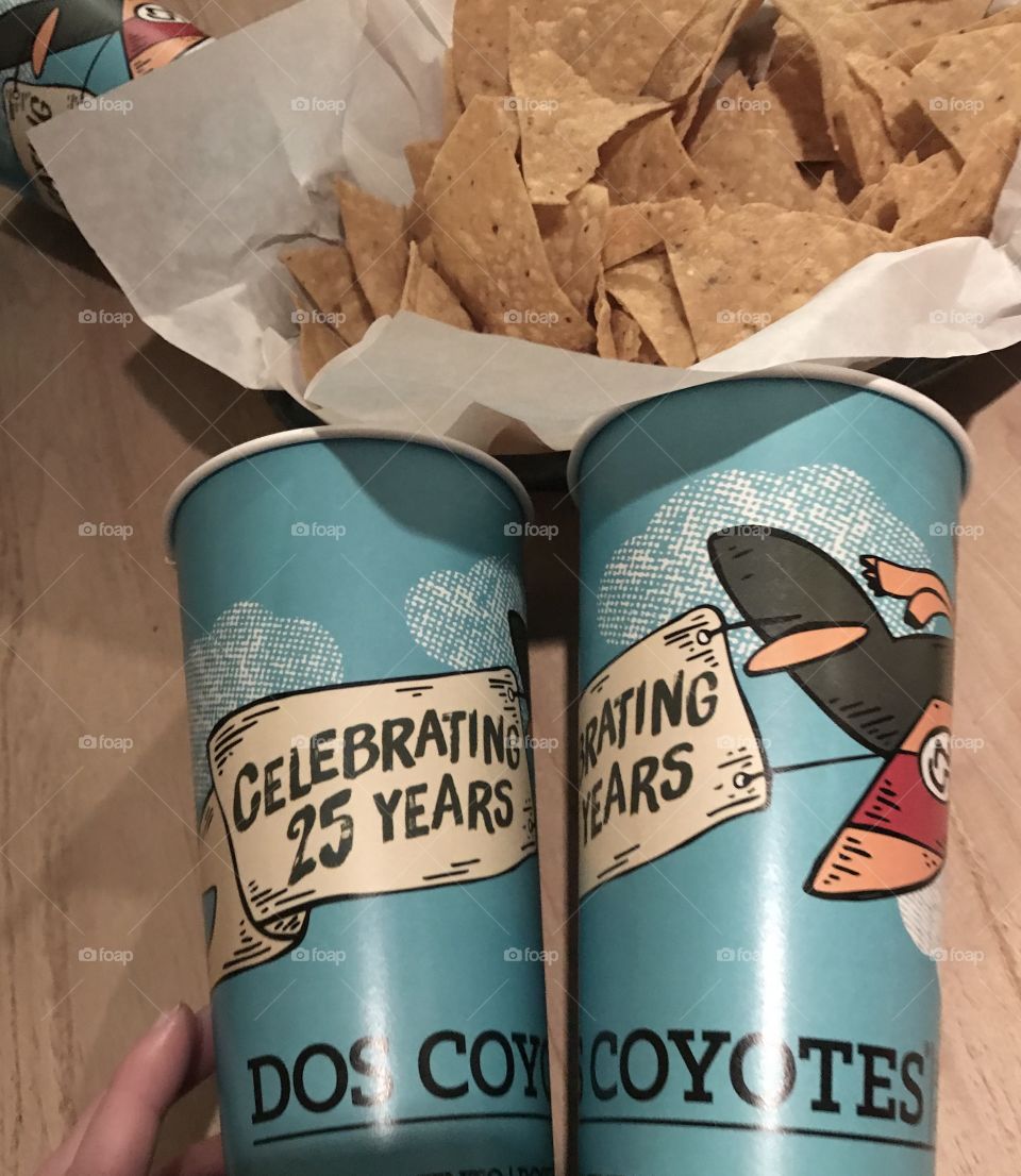 An image of two dos coyotes blue colored cups displayed next to a basket of tortilla chips at a restaurant in America, USA. 