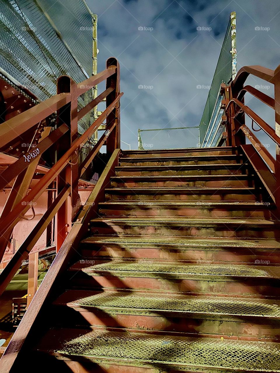This captivating nighttime view of an industrial minimalist red metal staircase with wrapped around shadows comes to us from the „Pulaski Bridge“ at „“Newtown Creek“ in LIC, Queens on a chilly evening in late December 2023. Hypnotic Productions