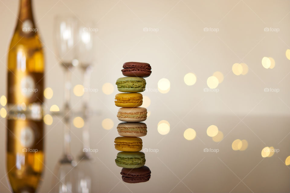 French macarons on a reflective  glass table top  with a bottle of champagne in the background 