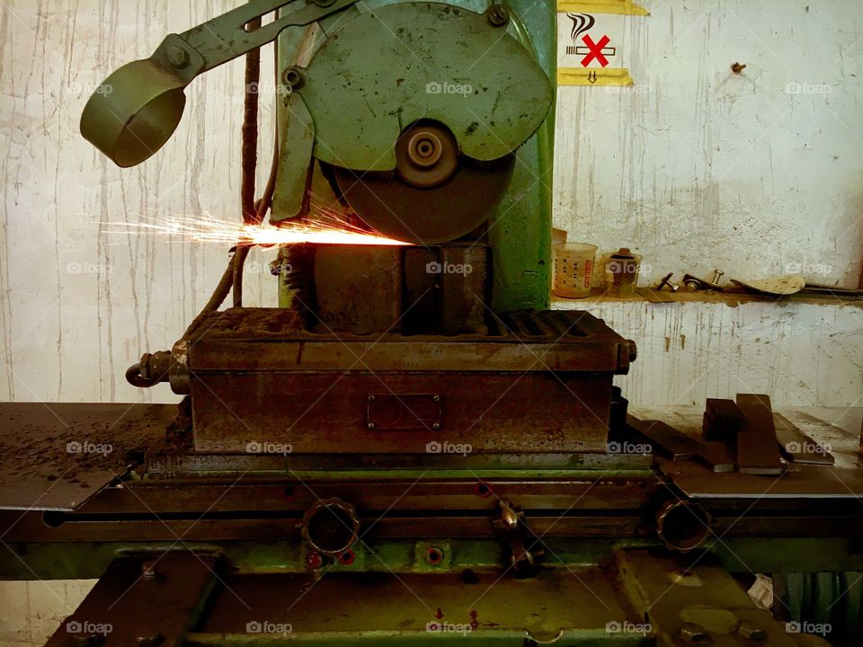 Vintage industrial sharpening machine from east Germany grinding a piece of steel. It is moving from side to side only and stands in an old hall in east Germany. It is about 60 years old.