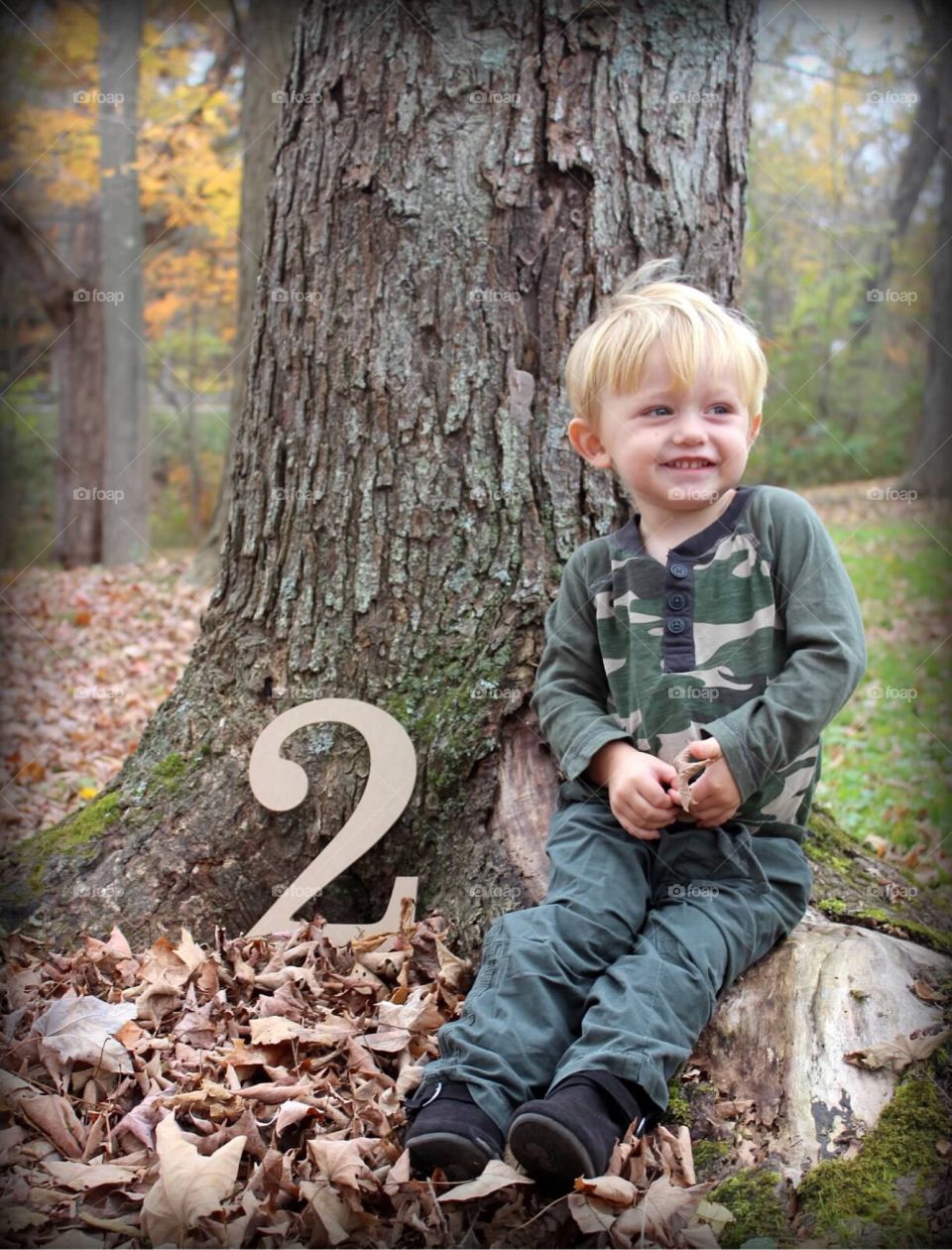 Cute boy sitting near tree trunk in the autumn