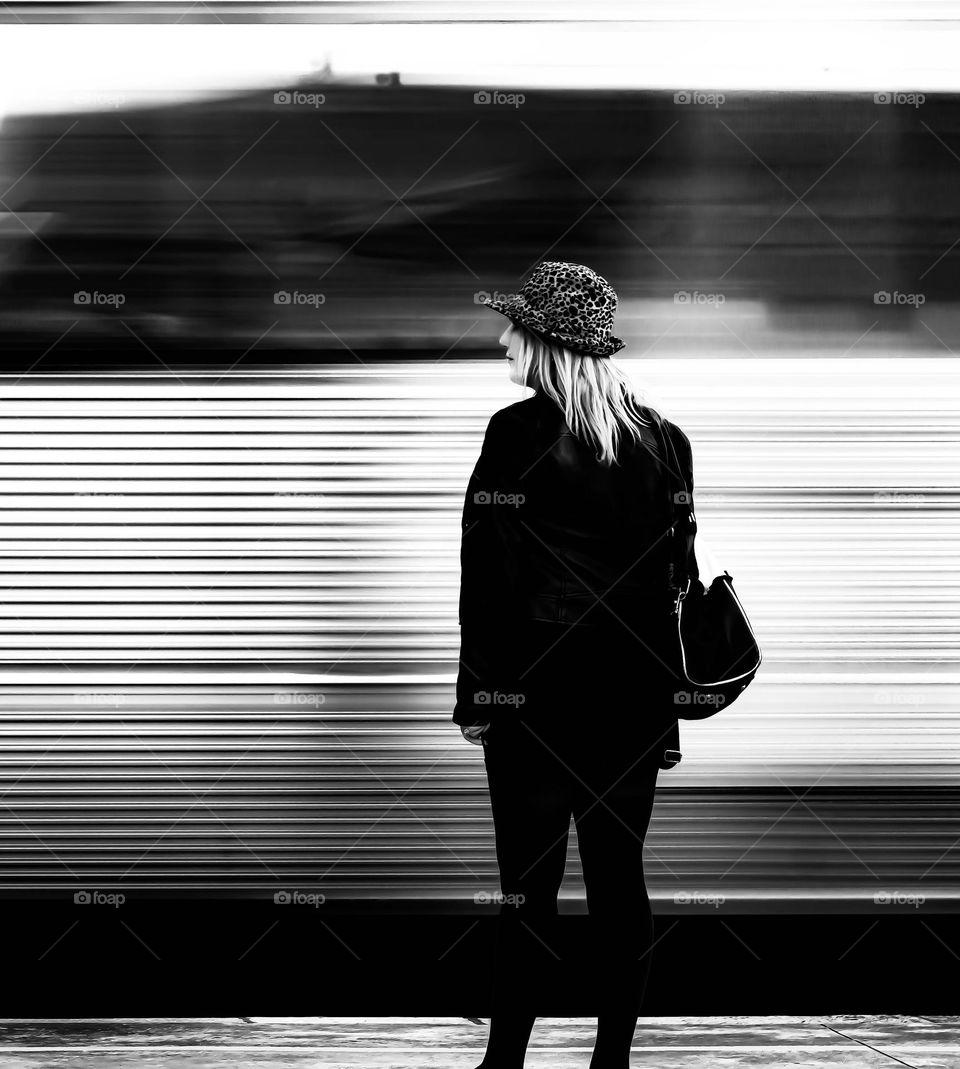 A woman stands on a platform as a train whizzes past