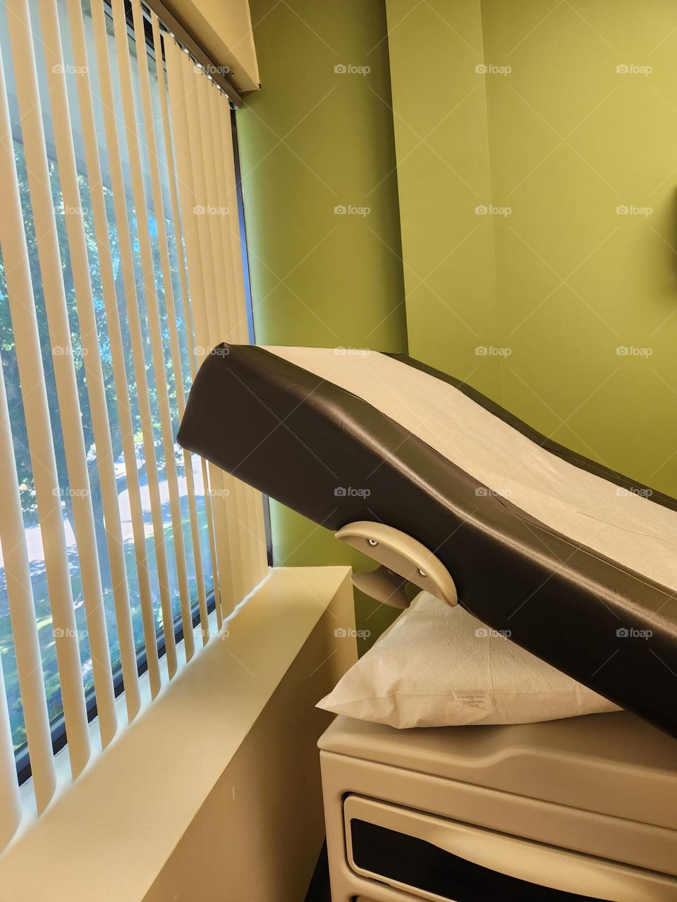 waiting inside a doctor's office with tilted patient seat, green wall, and slight view of the outside through the blinds