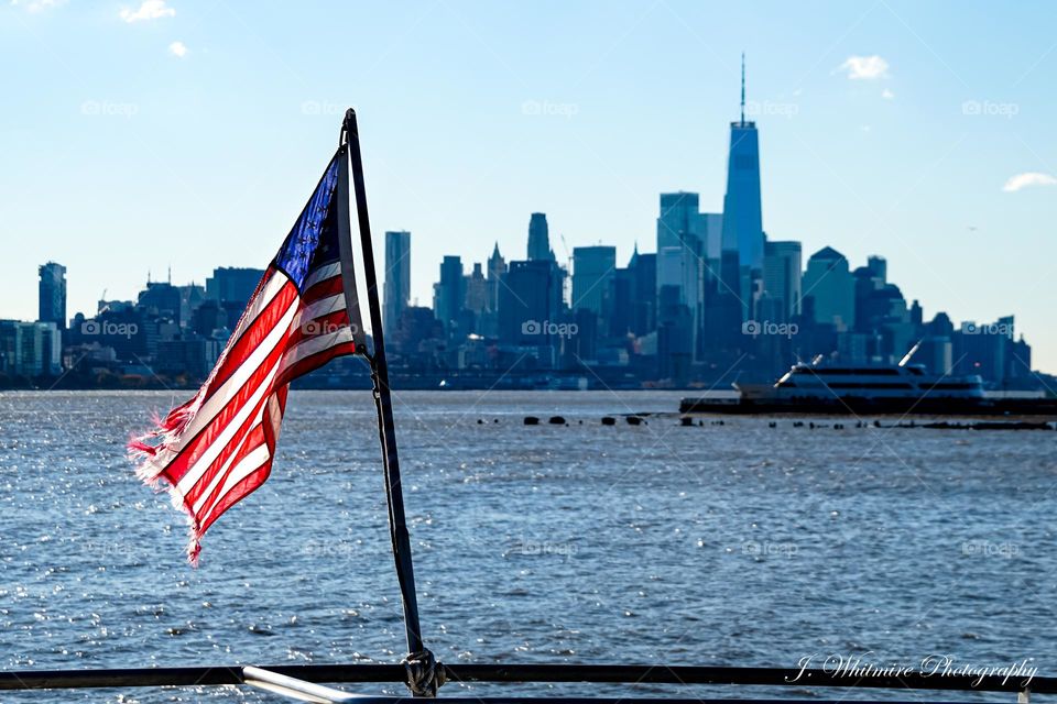 An American flag waves in the foreground as the skyline of Manhattan appears in the background