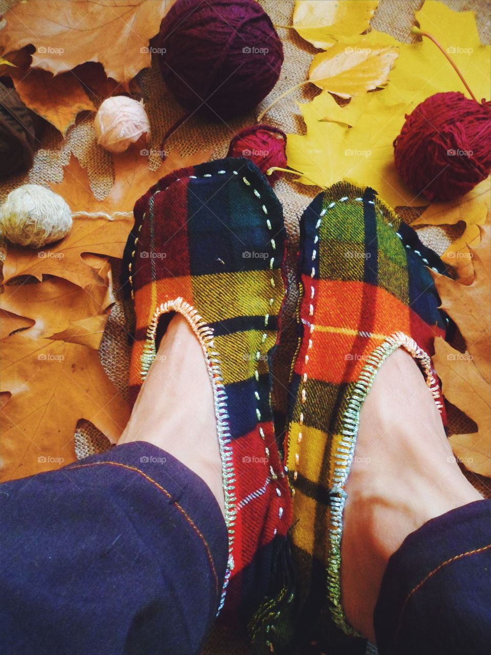 warm homemade slippers with their hands on the background of autumn leaves