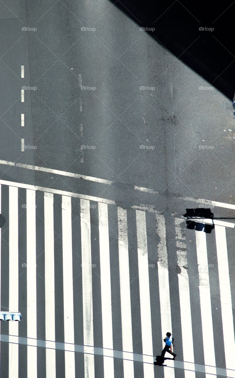 A person runs across a monochrome pedestrian crossing in Tokyo. There are shadow and geometric lines. 