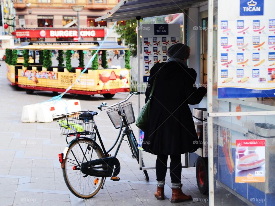 Woman and bicycle about to by a sausage on the street