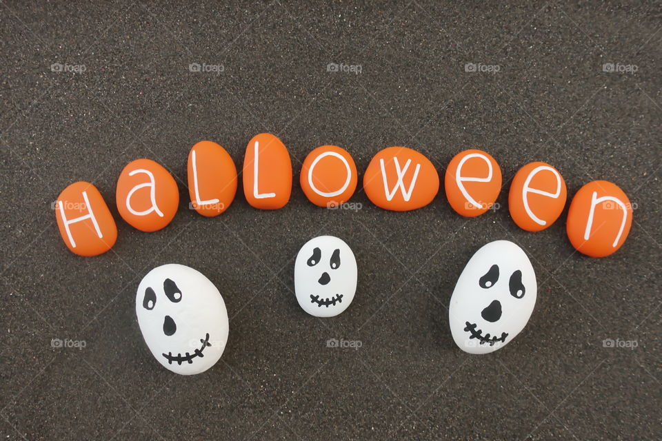 Halloween, orange painted stones with ghosts over black volcanic sand