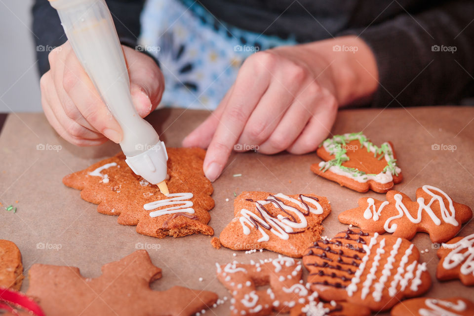 Woman decorating baked Christmas gingerbread cookies with frosting