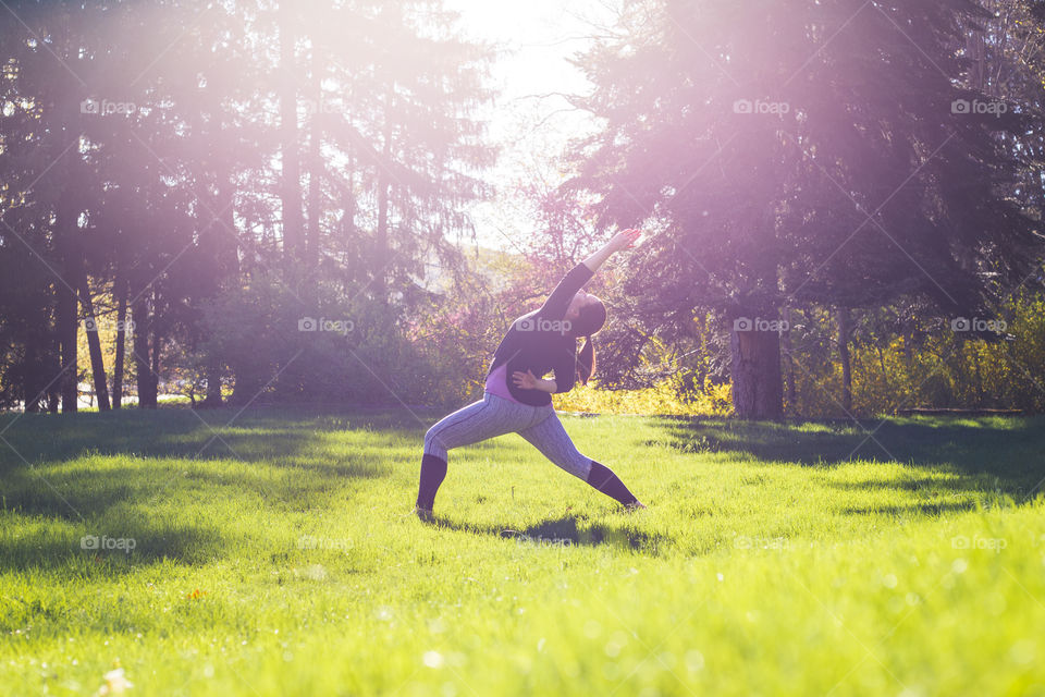 A yoga teacher practices warrior poses in the middle of a field during spring as golden hour starts and she glows connected to nature